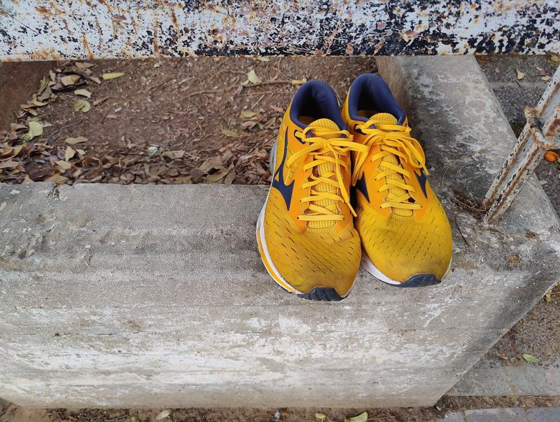 A pair of Mizuno Wave Rider 24 in bright golden yellow with black accents and white sole, placed on weathered concrete steps waiting to be adopted